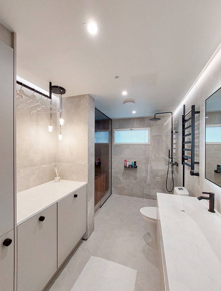 Une salle de bains avec une surface lumineuse éclairée par des downlights et un bandeau de leds montés au plafond et sur les longs côtés du plafond. Lampe suspendue supplémentaire.